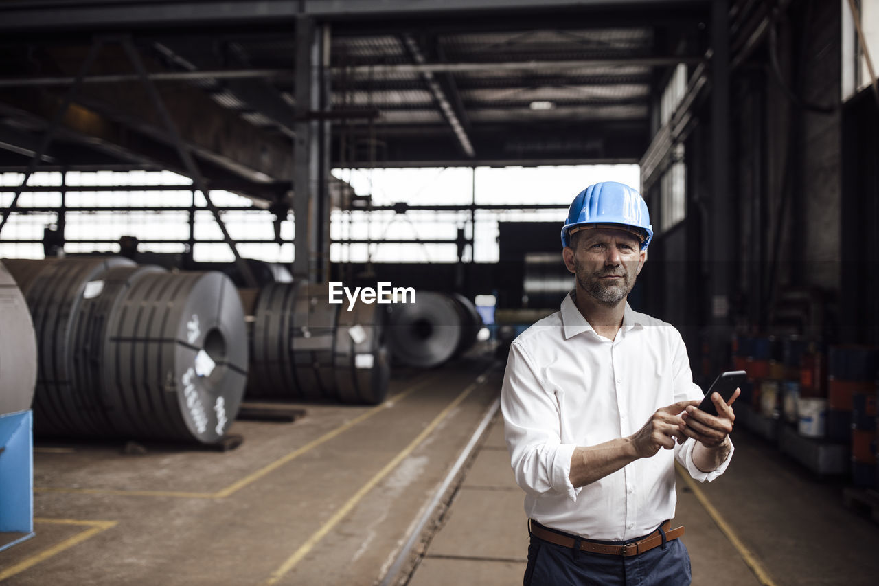 Businessman holding smart phone while standing in factory