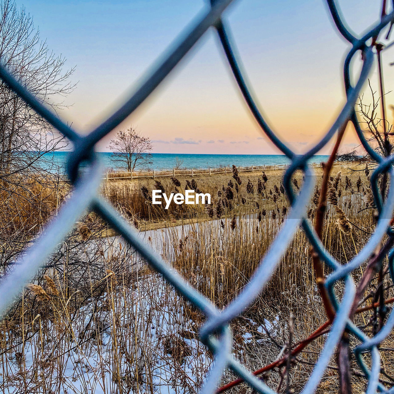 CHAINLINK FENCE BY SEA AGAINST SKY SEEN THROUGH METAL GRATE