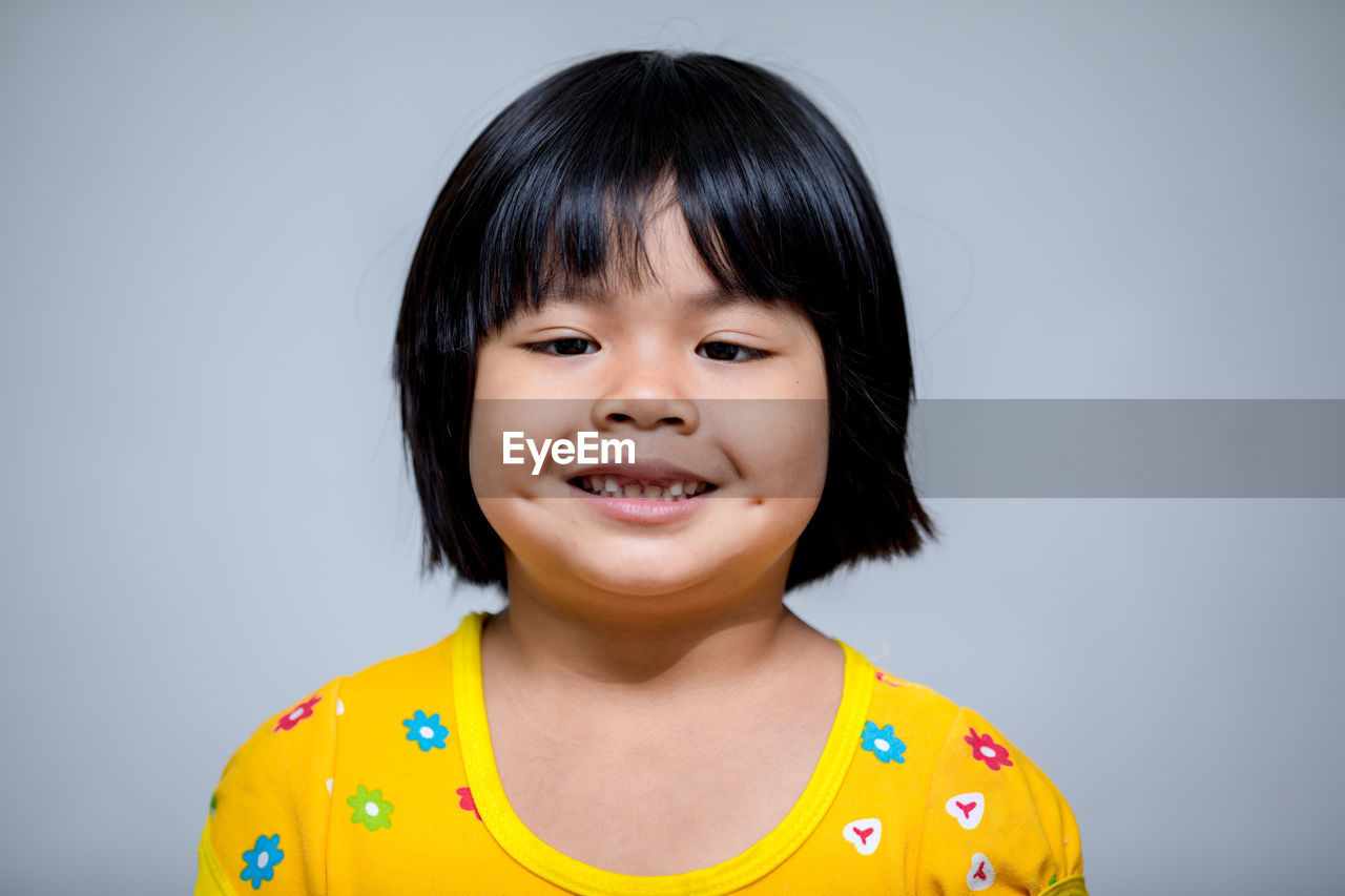 Close-up portrait of smiling cute girl against gray background