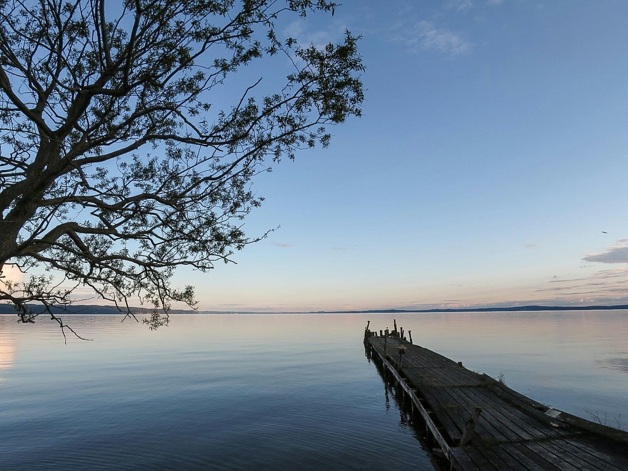 Pier over river against sky at sunset