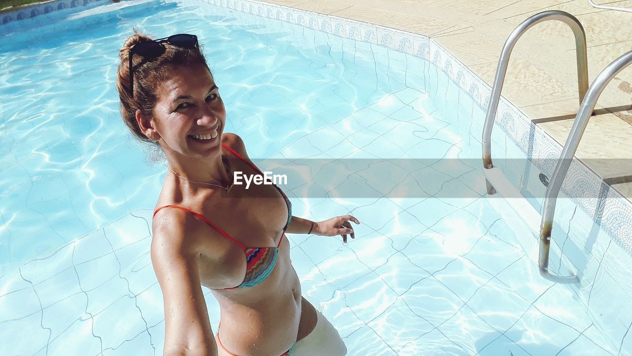 High angle portrait of smiling woman wearing bikini in swimming pool