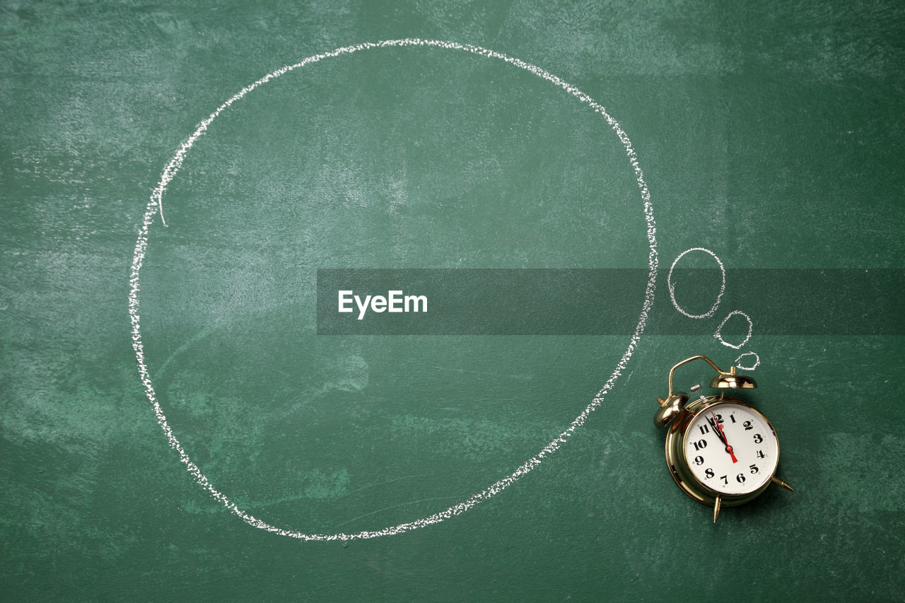 Directly above shot of alarm clock with speech bubble on blackboard