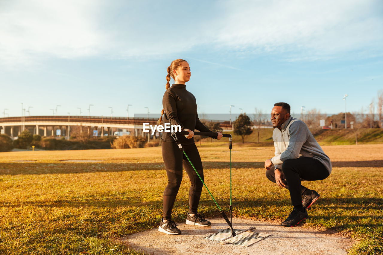 Woman pulling belt by instructor on land against sky in sunny day