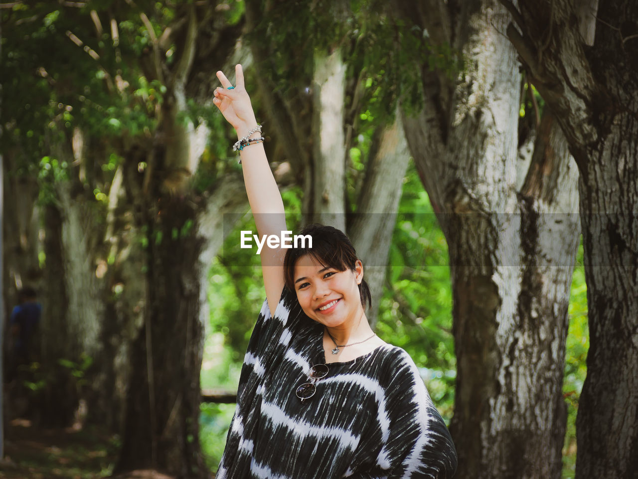 Portrait of smiling young woman standing against tree trunk