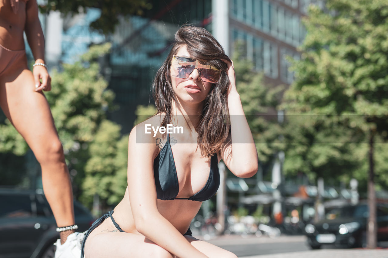 Portrait of young woman wearing sunglasses and bikini in city during sunny day