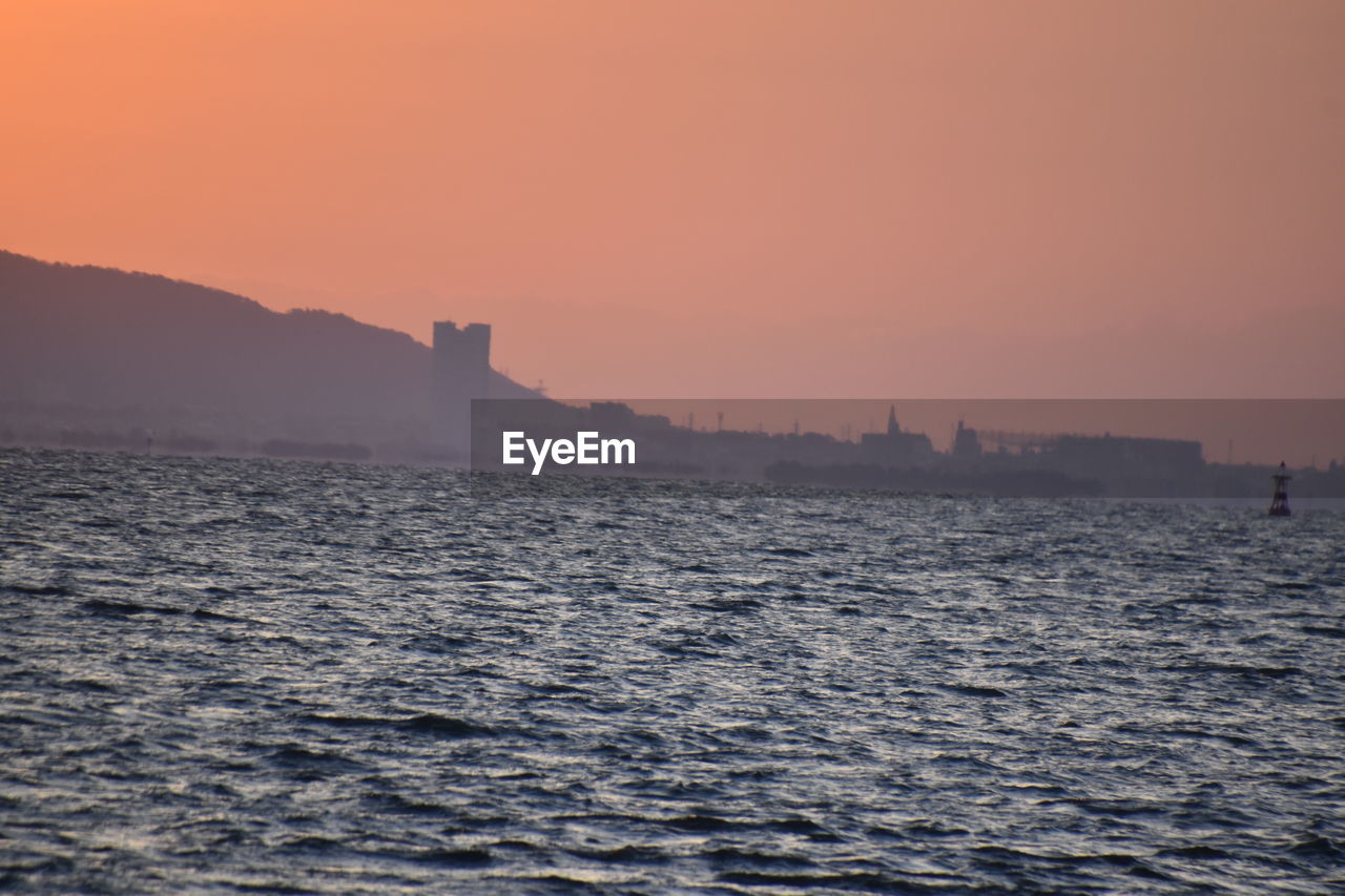 SCENIC VIEW OF SEA AGAINST BUILDINGS DURING SUNSET