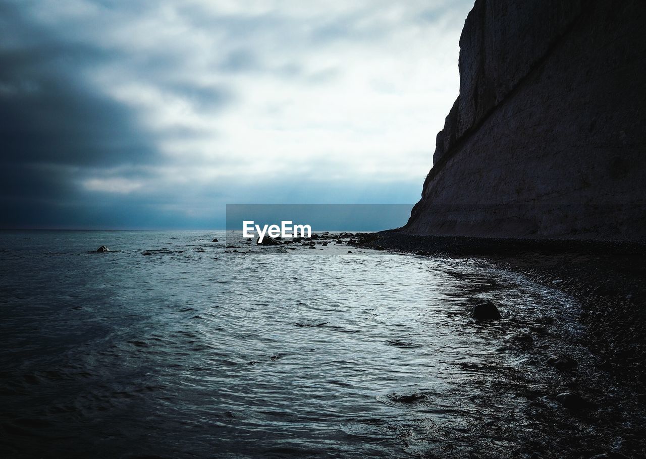 Scenic view of sea by cliff against cloudy sky