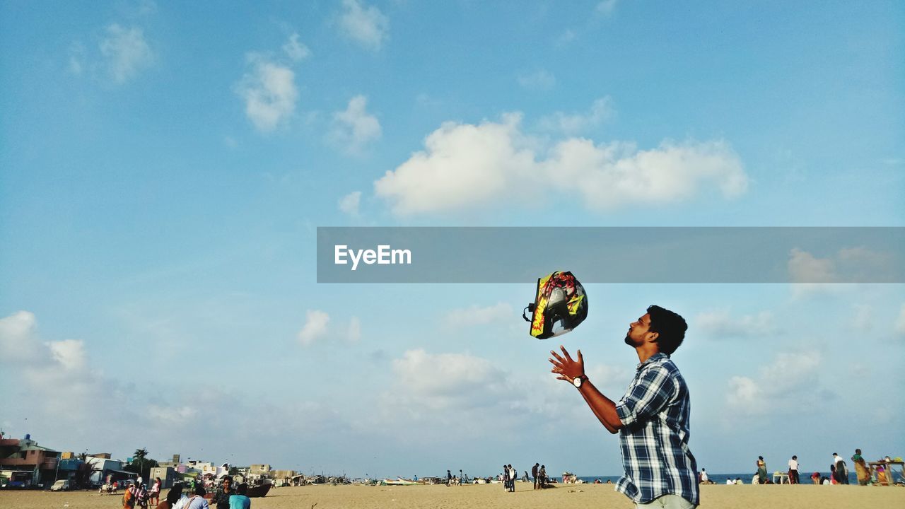 Man throwing helmet against sky