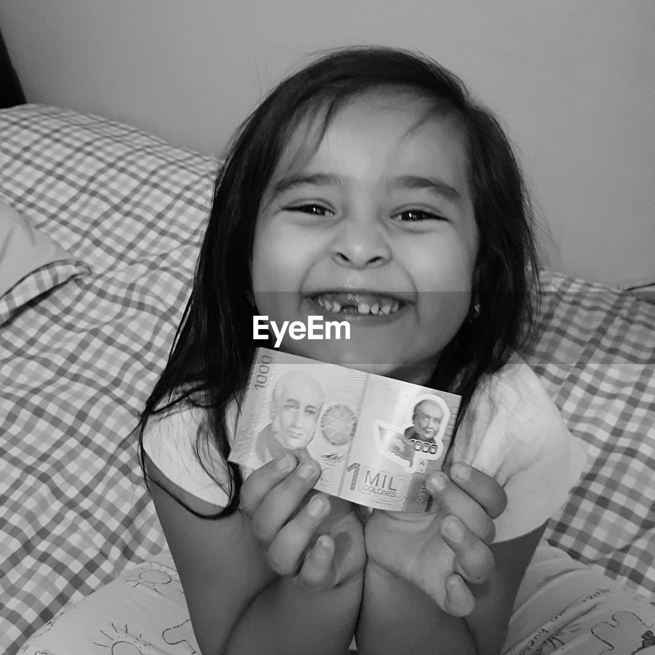 Portrait of cute girl holding currency note while sitting on bed