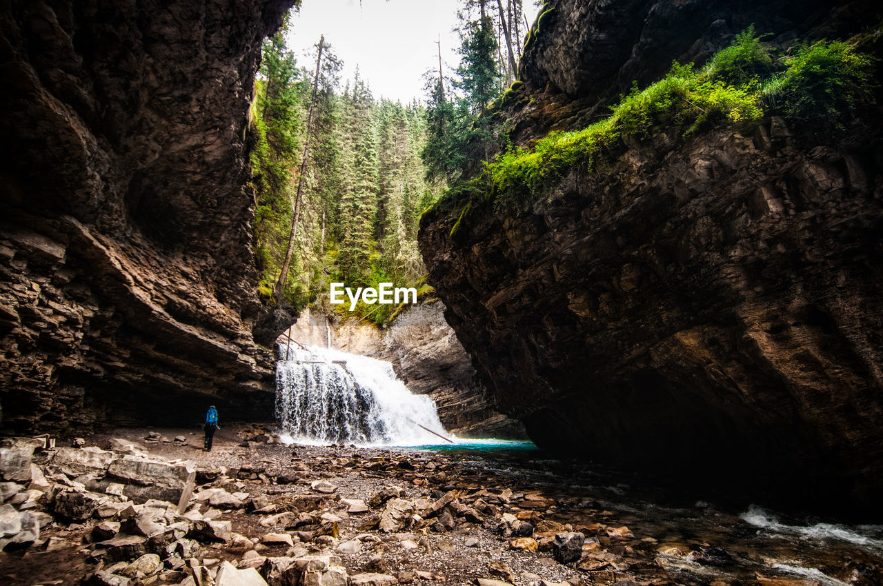 Distant view of female hiker walking against waterfall in forest