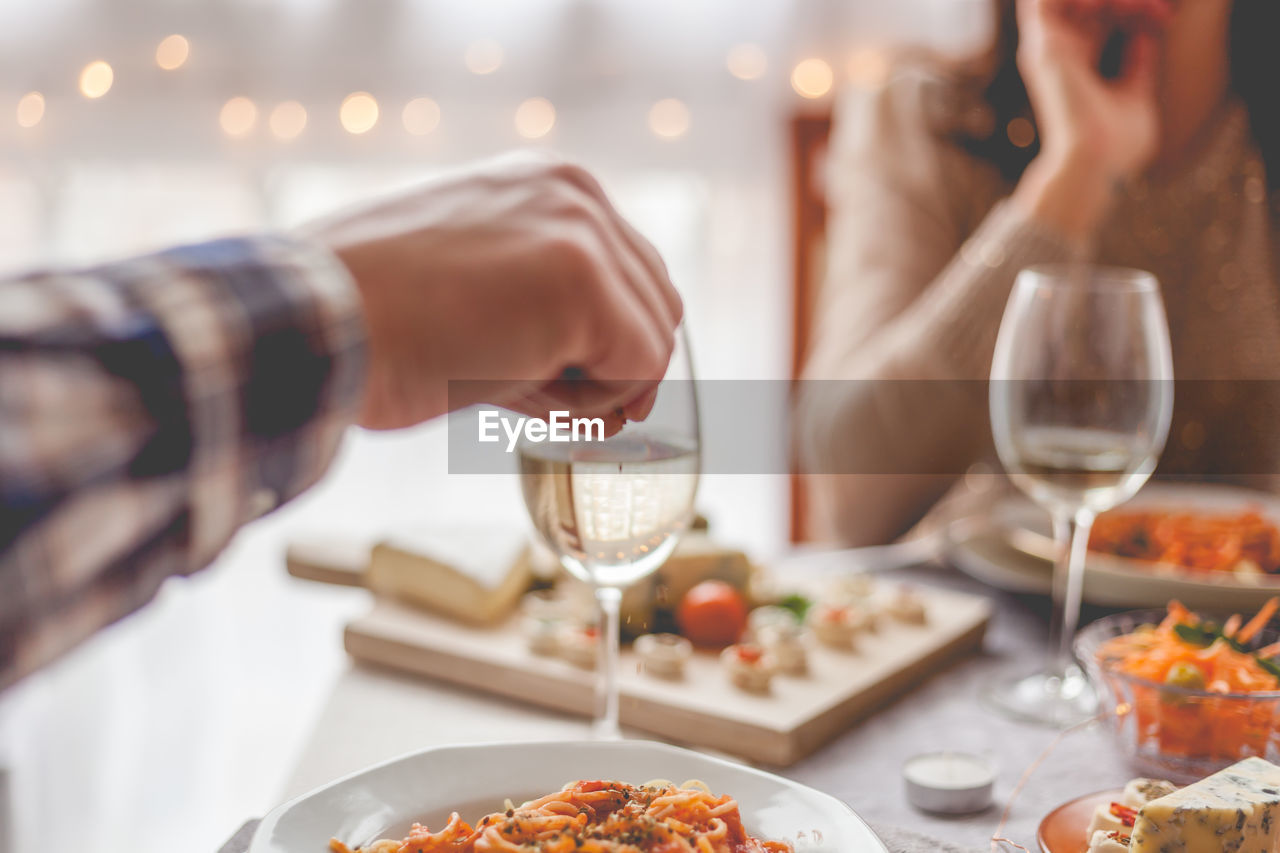 Close up of unrecognizable man seasoning his pasta during lunch at dining table.