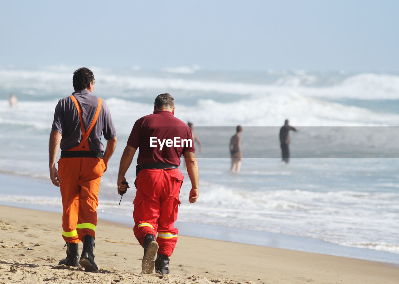 Rear view of men walking at beach