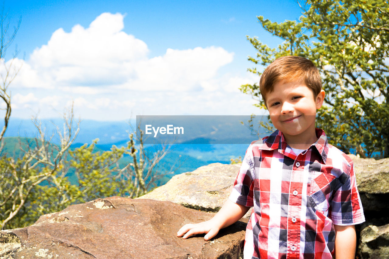 Portrait of smiling boy standing by trees against sky