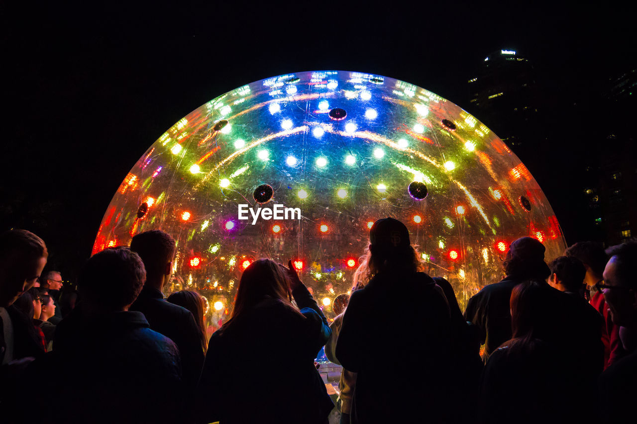 Rear view of people standing by large illuminated ball in nightclub