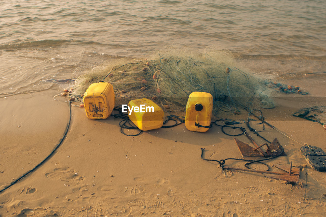 High angle view of yellow toy on beach fishing net and empty canisters on the sand 