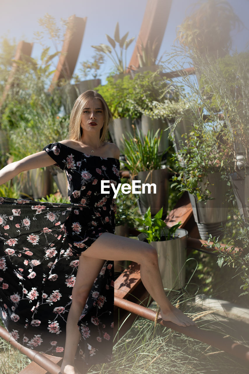 YOUNG WOMAN SITTING ON PLANT IN GARDEN