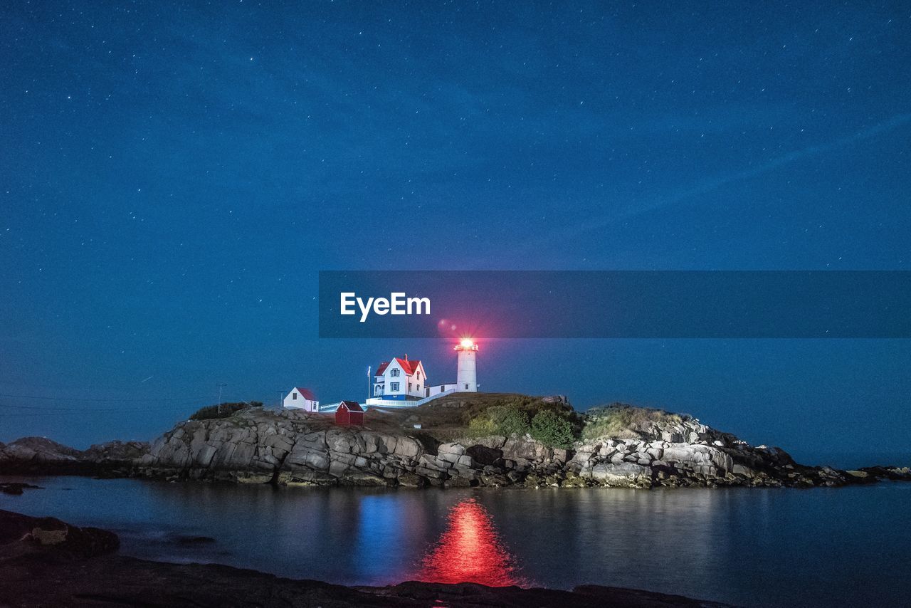 Illuminated nubble lighthouse by sea against star field