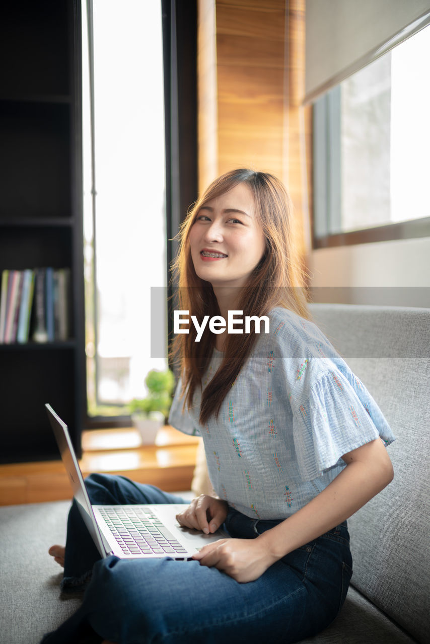 Side view of smiling woman using laptop on sofa at home