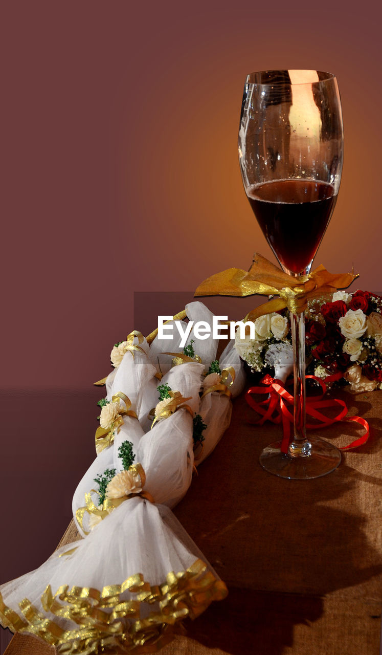 CLOSE-UP OF WINE GLASS ON TABLE AGAINST RED WALL