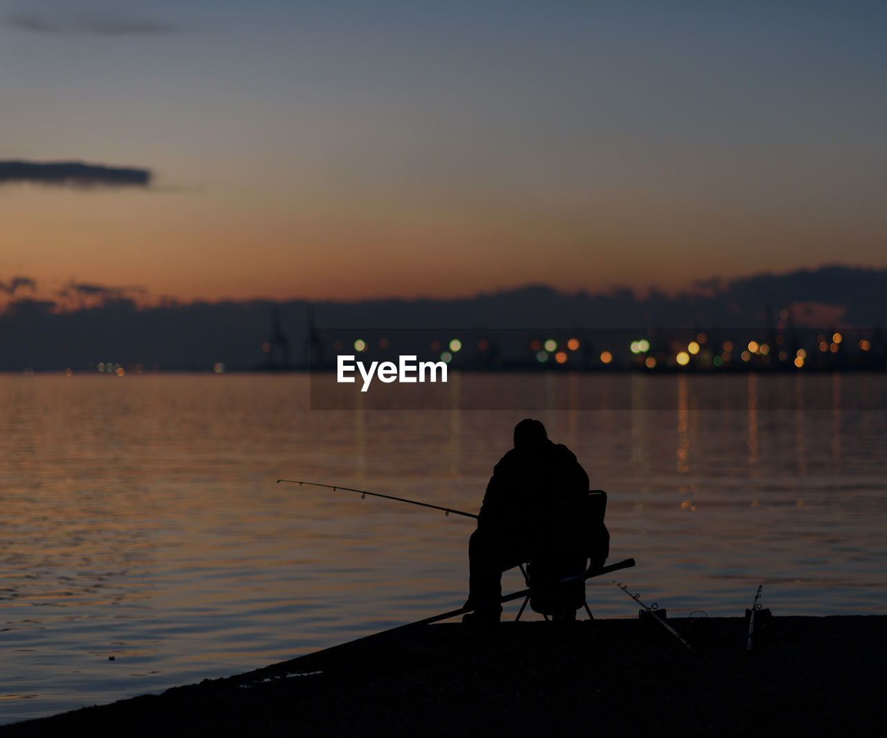 Rear view of silhouette man fishing in sea against sunset sky 