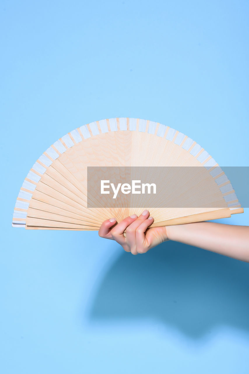 Close-up of woman holding hand fan against blue wall