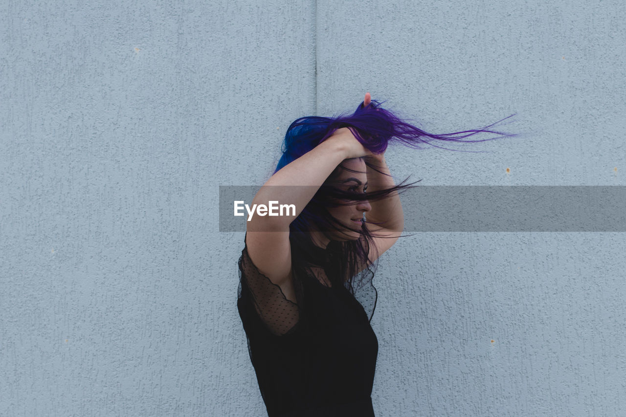 Smiling woman with dyed hair standing against wall