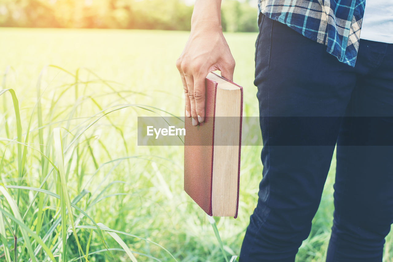 Midsection of man holding book while standing on field