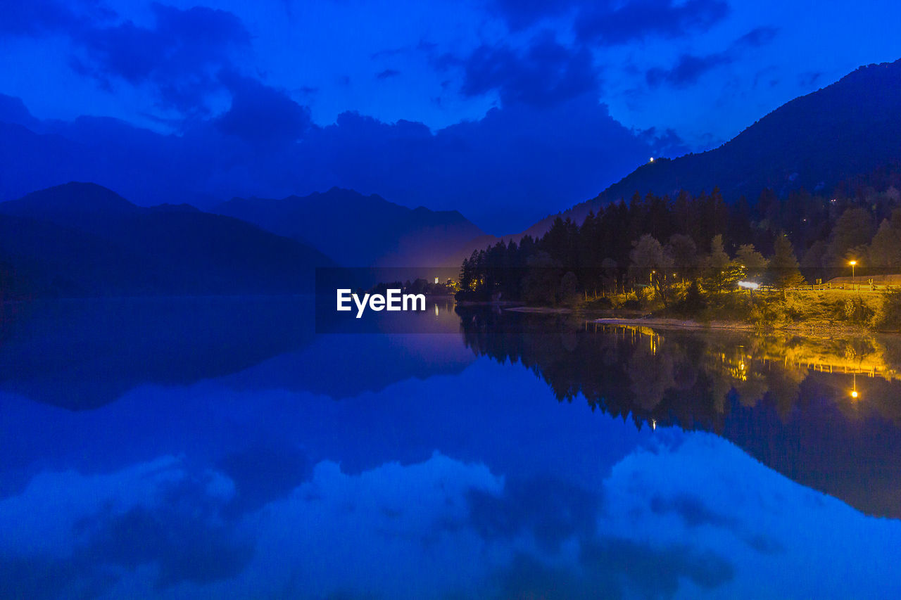 Scenic view of lake by mountains against blue sky at dusk