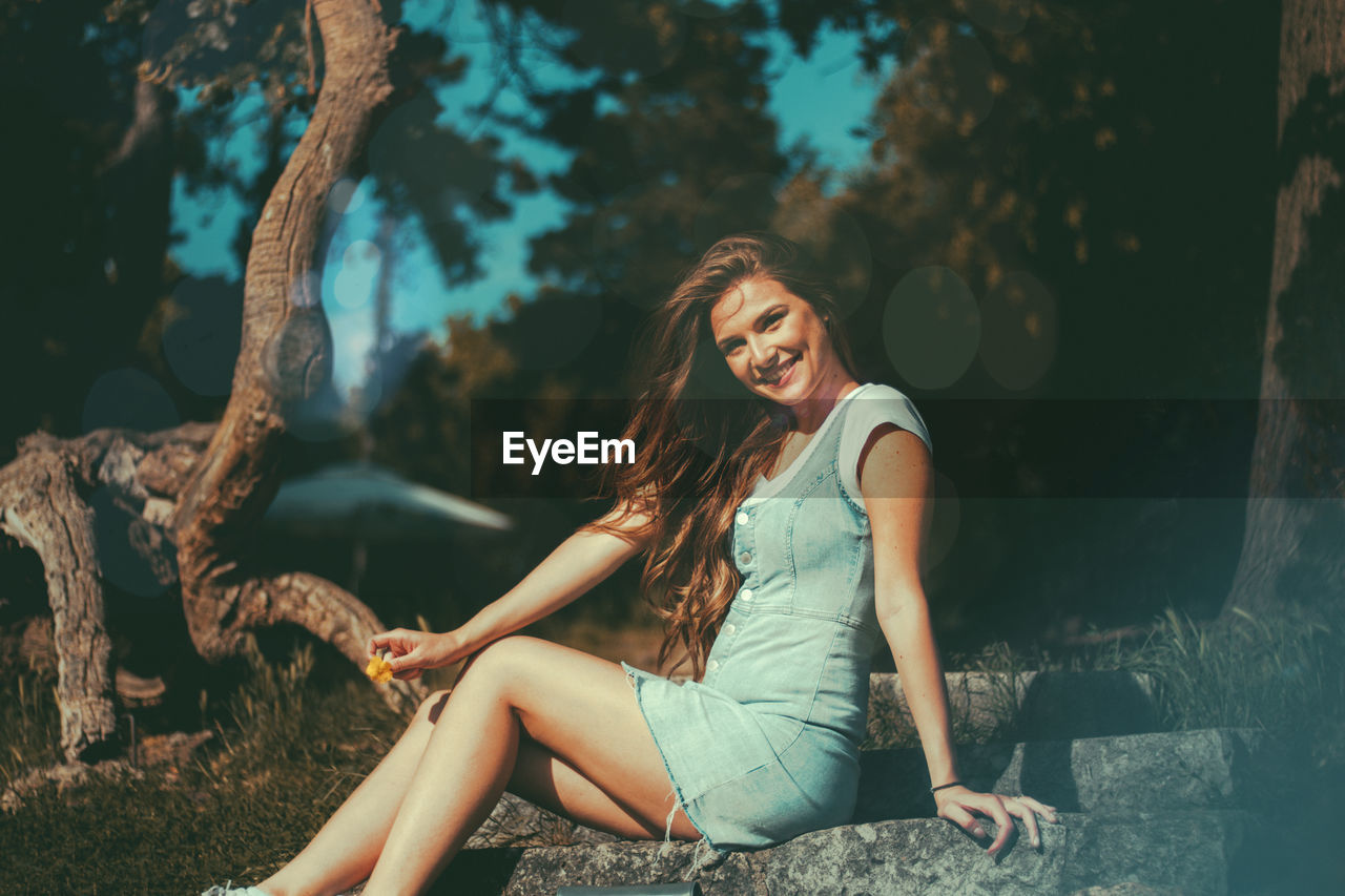 Young woman sitting by tree against plants