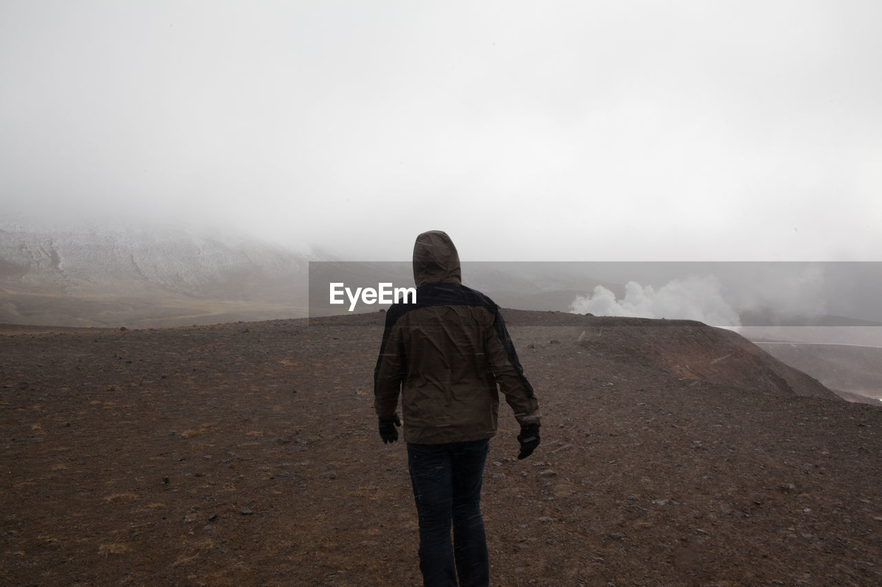 Rear view of tourist walking on arid landscape against clear sky