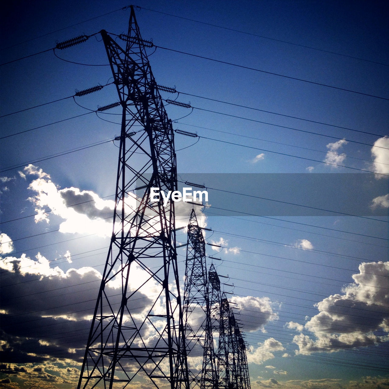 Low angle view of electricity pylons against blue sky and clouds
