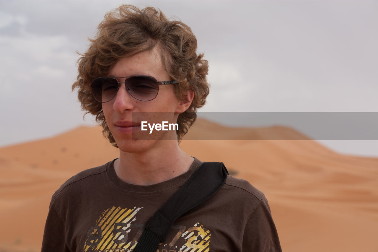 Young handsome man wearing sunglasses standing in desert