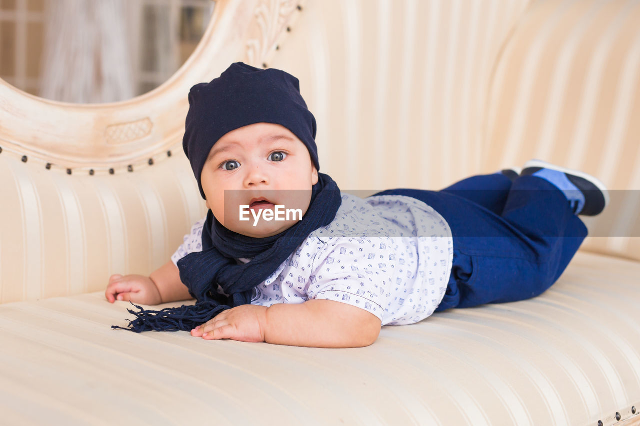 portrait of cute baby boy sitting on bed at home