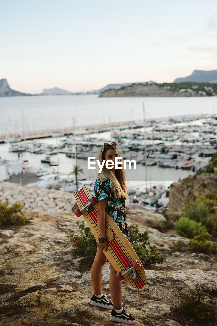 Young female with long board skate in front of moraira's yacht club