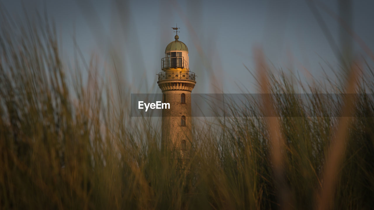 Lighthouse by plants against sky during sunset