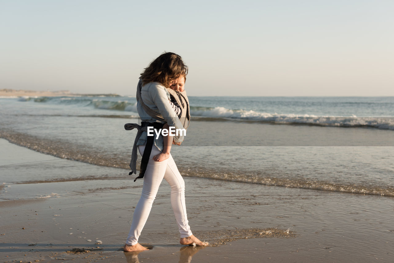 Mother carrying son while walking at beach