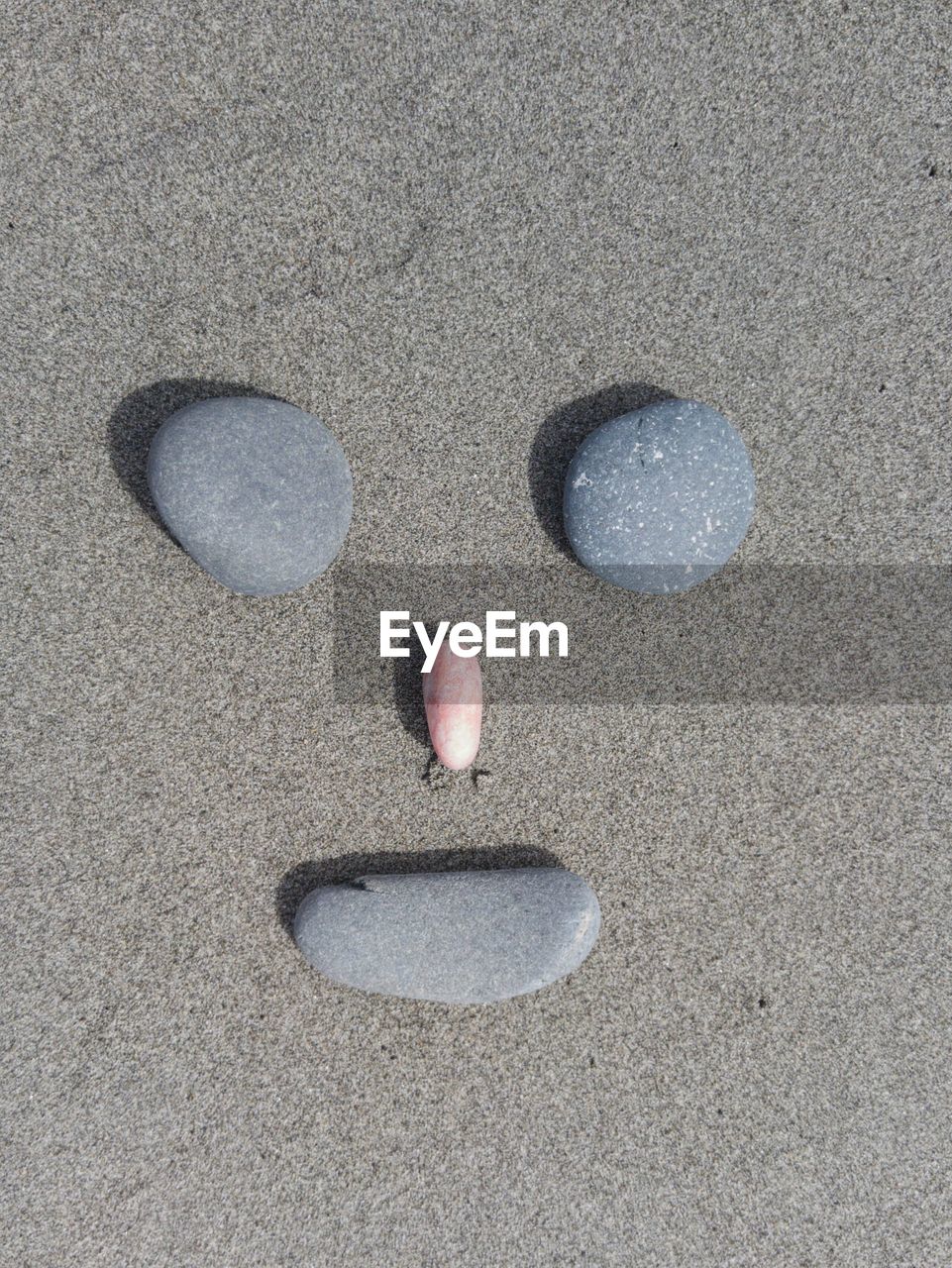 High angle view of anthropomorphic face made from pebbles on sand at beach