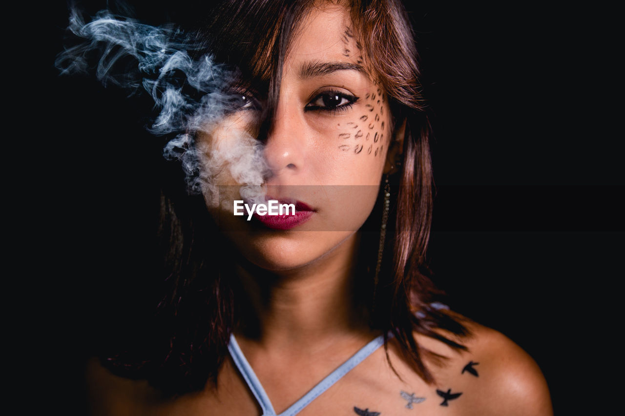 Portrait of young woman exhaling smoke against black background