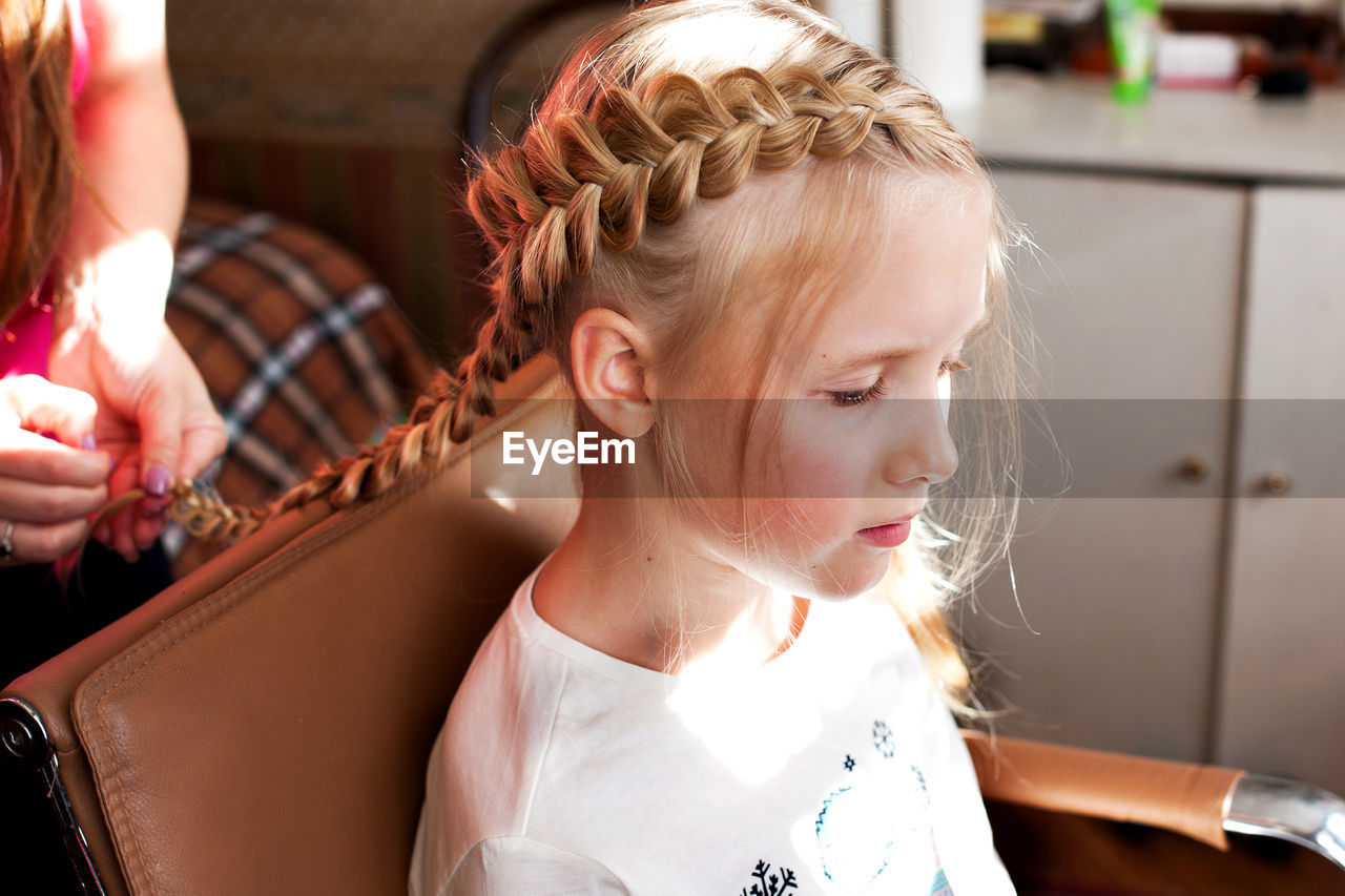 Close-up beautician braiding hair of girl 