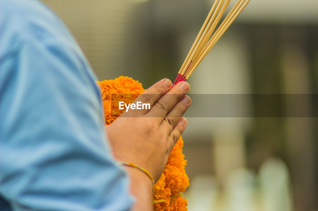 Cropped hands holding incense sticks with floral garland in temple