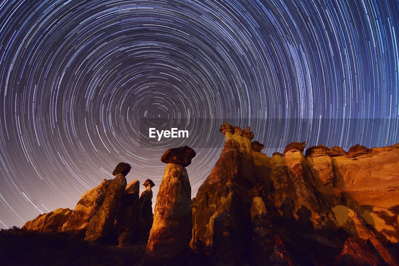Low angle view of rock formations against star trail