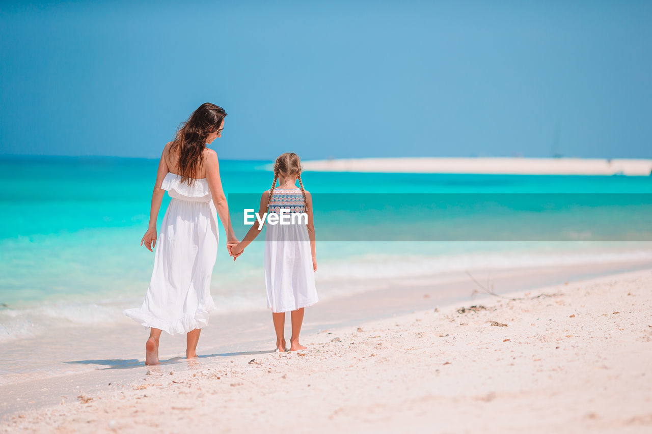 Rear view of mother and daughter holding hand on beach