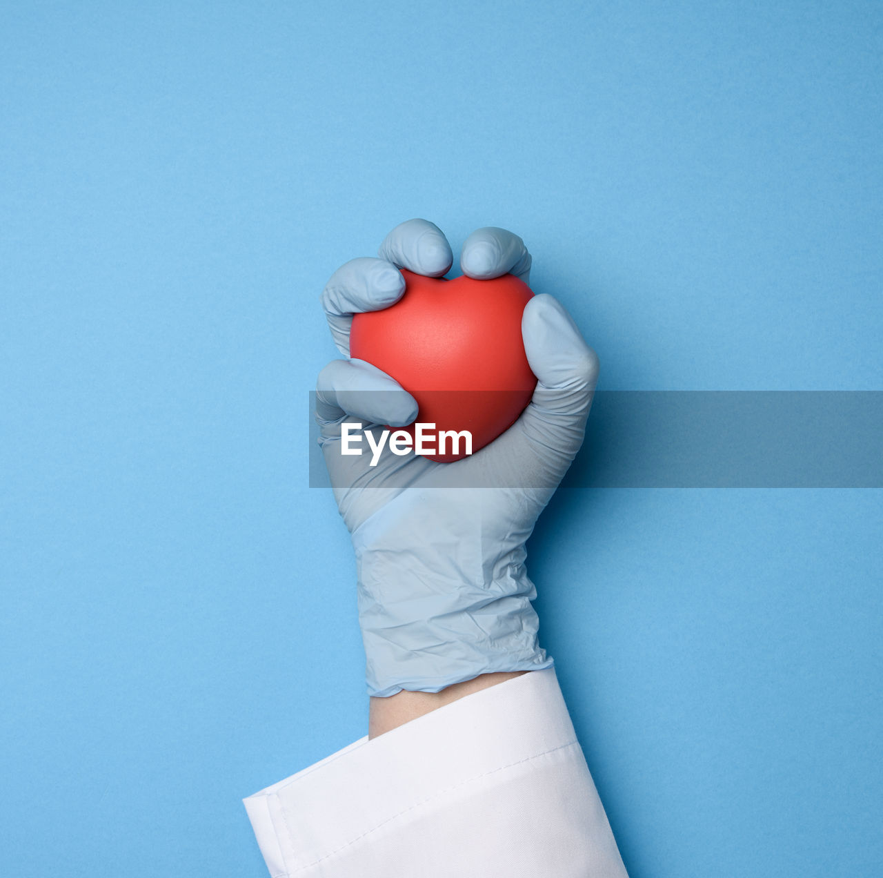 Female hand in blue latex gloves holding a red heart, donation concept, top view