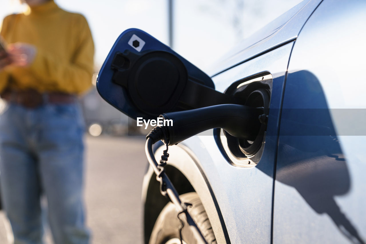 Electric car charging at station with woman standing in background