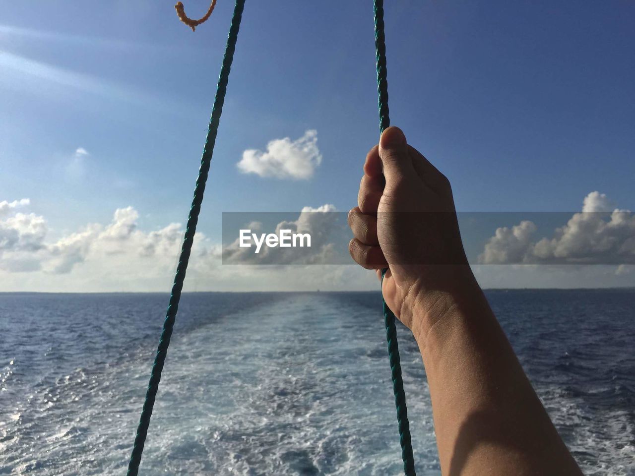 Close-up of hand holding rope against sky