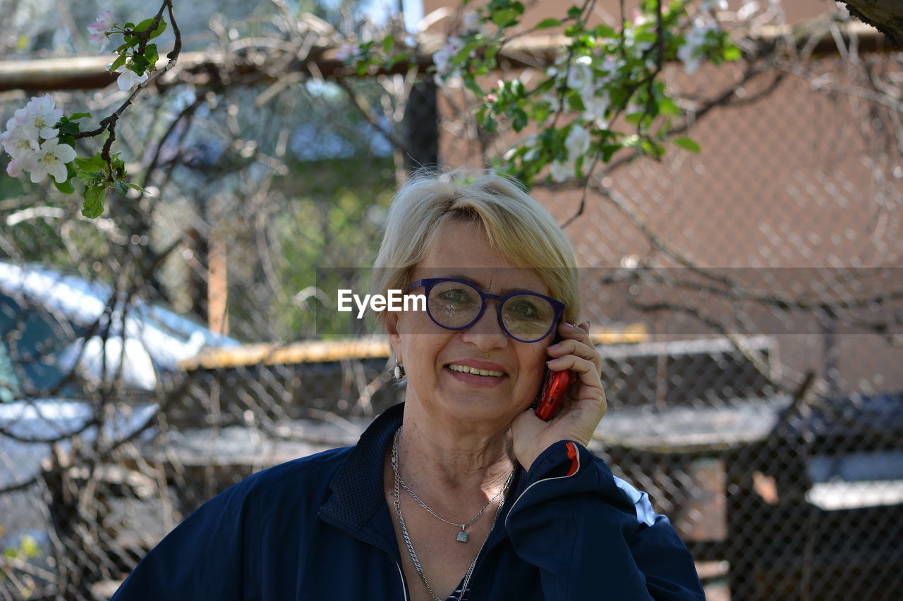 Portrait of smiling woman talking on phone while standing by tree