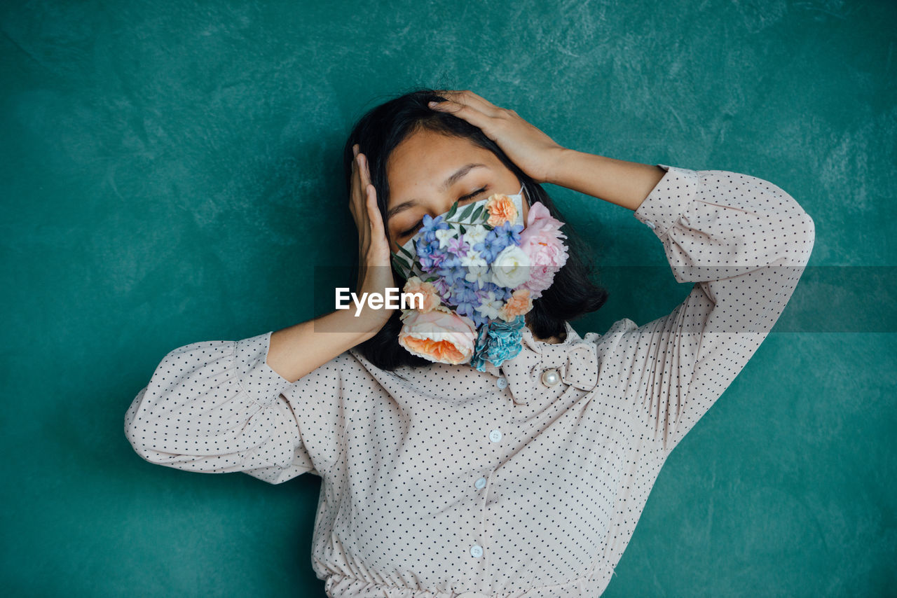 Woman covering mouth with flowers against blue wall