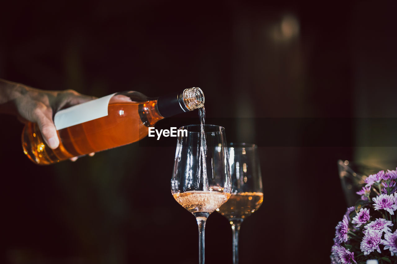 Man pouring rose wine from bottle into glass indoors.