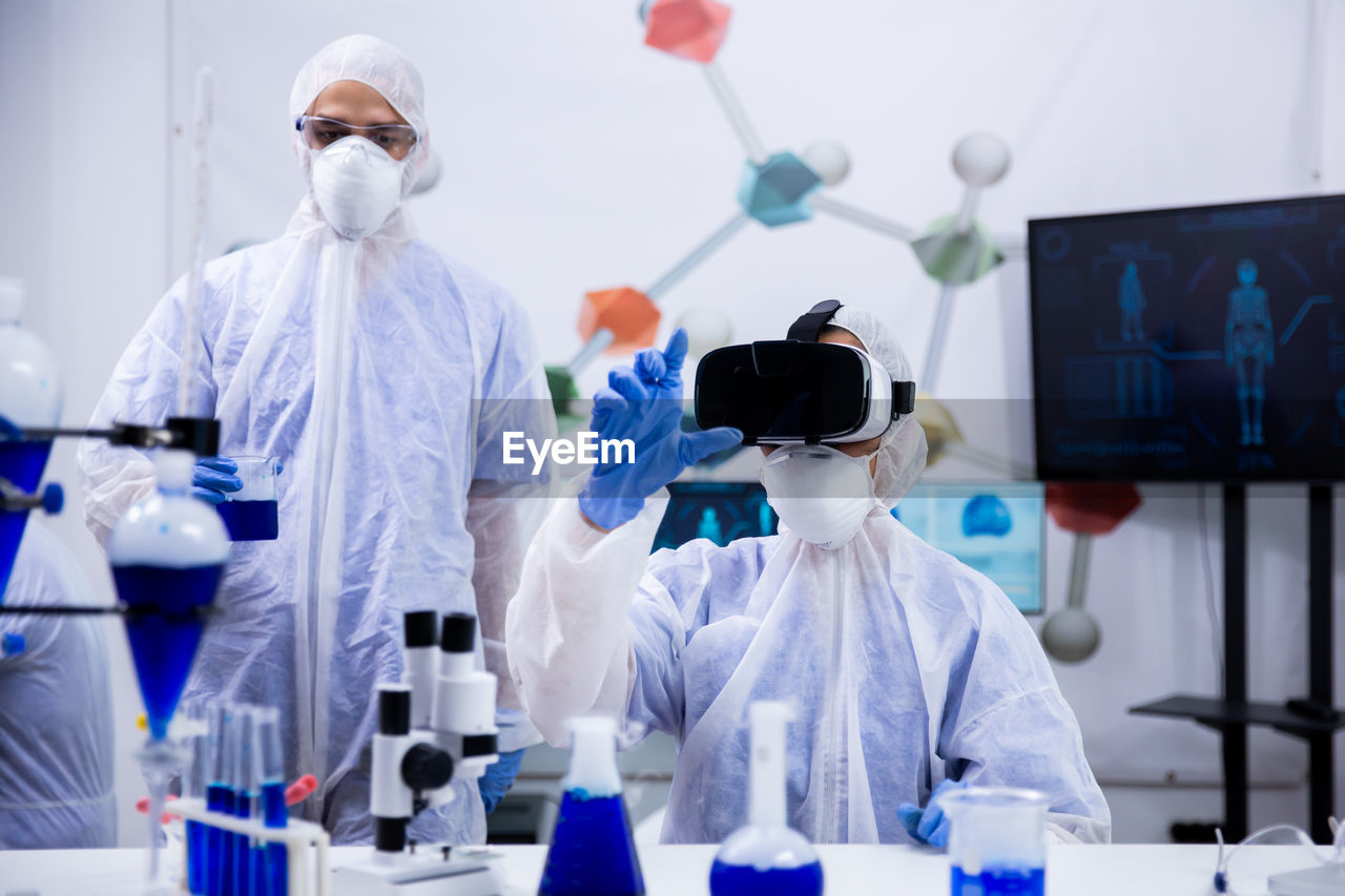 Scientist wearing virtual reality simulator colleague in background at laboratory