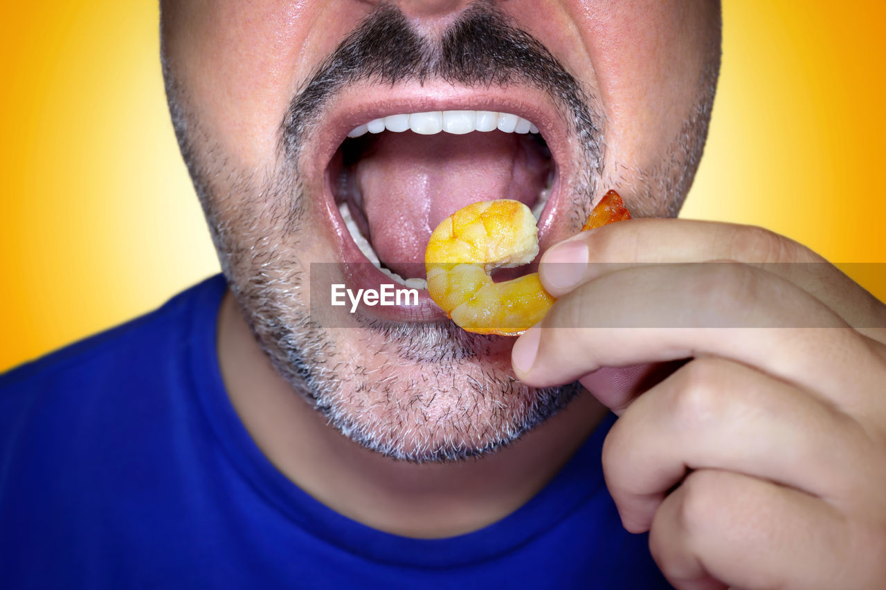 Close-up of a hungry man biting into a prawn. irresistible craving for food. yellow background.